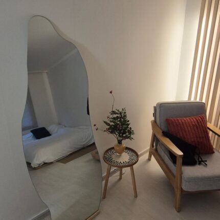 A cozy minimalist bedroom featuring a large mirror, elegant armchair, and a touch of greenery.